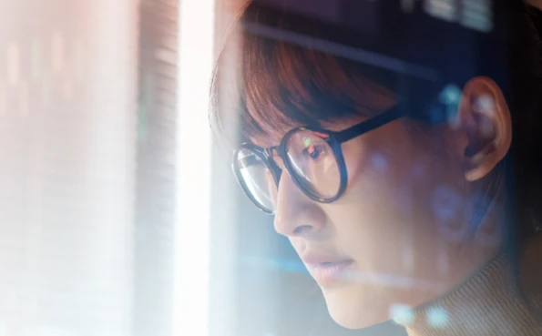 Digital analyst working in a bright office; the reflection on her glasses shows data flows monitored for cybersecurity and network protection.