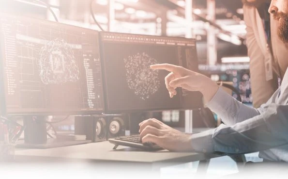 Two data professionals collaborate on a dual-monitor computer, analyzing complex 3D data models and AI applications.