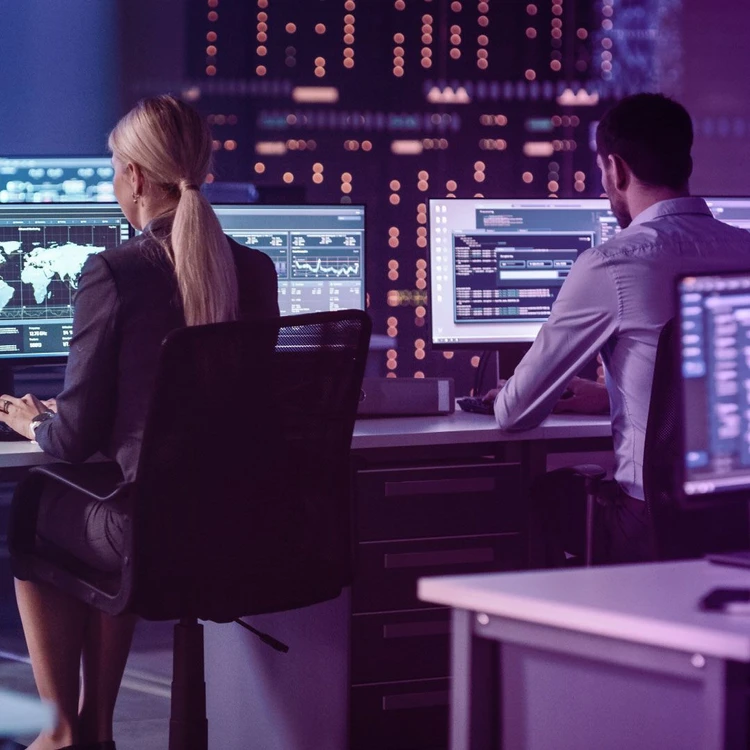 A man and a woman, sitting at their workstations in the office, look at computer monitors.