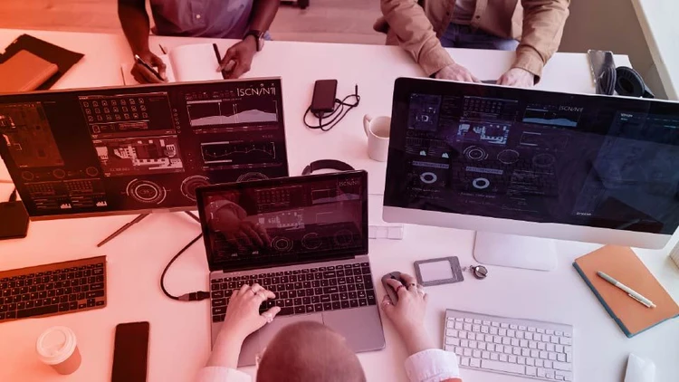 Team engaged in software development, with code, data, and analysis interfaces displayed on multiple laptops and monitors.