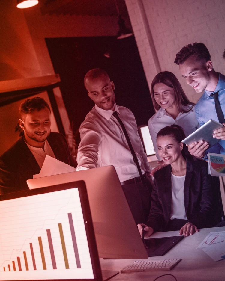 A team of professionals collaborating in front of a monitor displaying growth charts and data analysis in a modern office.